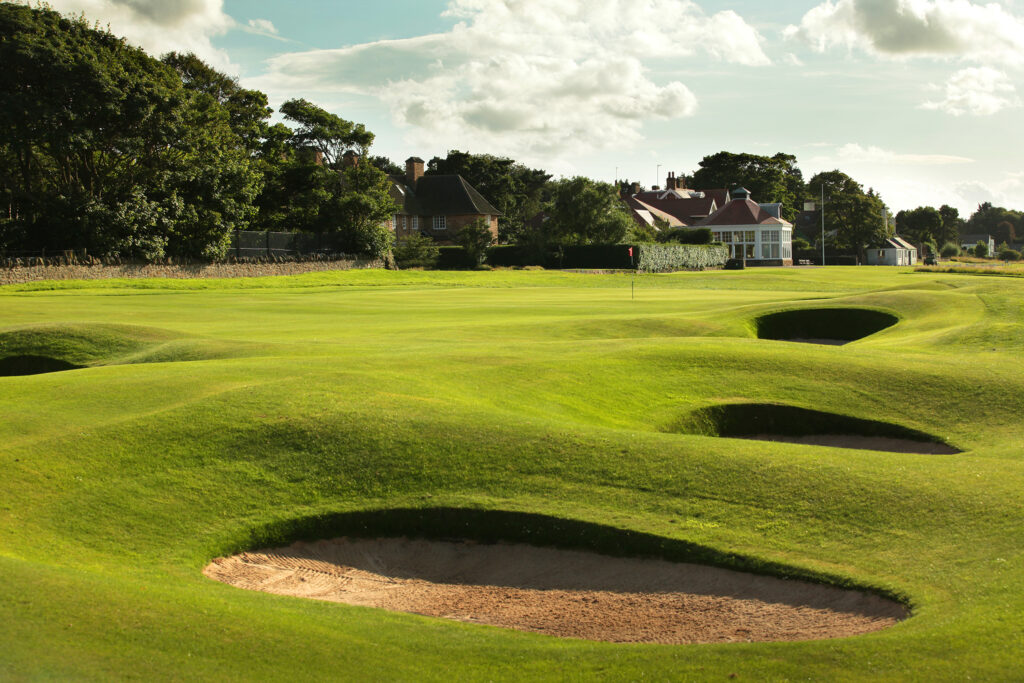 Hole with bunkers at Muirfield with building in background and trees around