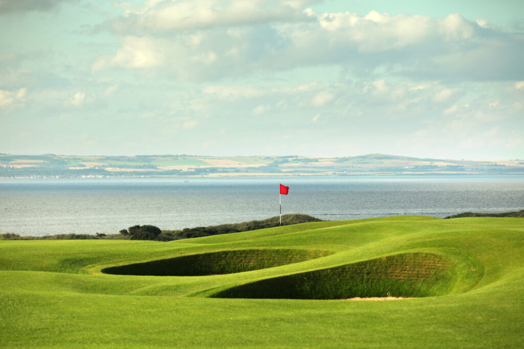 Hole with red flag and bunkers at Muirfield with ocean in background