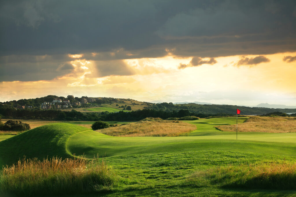 Hole with red flag at Muirfield with fairway and trees in background