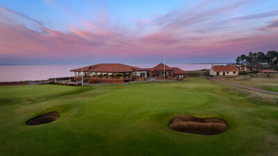 Hole with bunkers at Nairn Golf Club with building in background at sunset