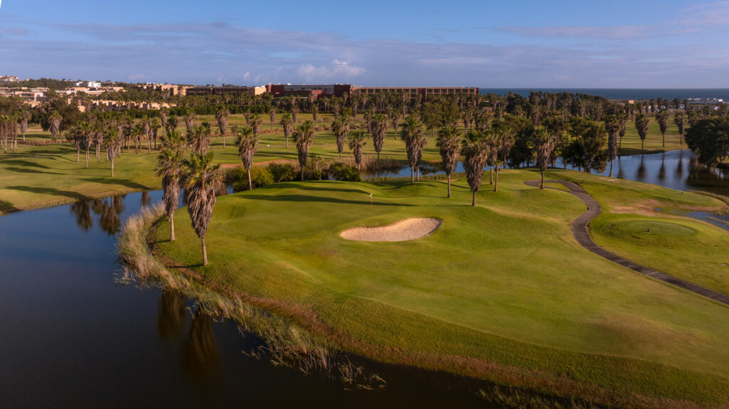 A hole surrounded by water hazard and bunker with palm trees at Salgados Golf Course