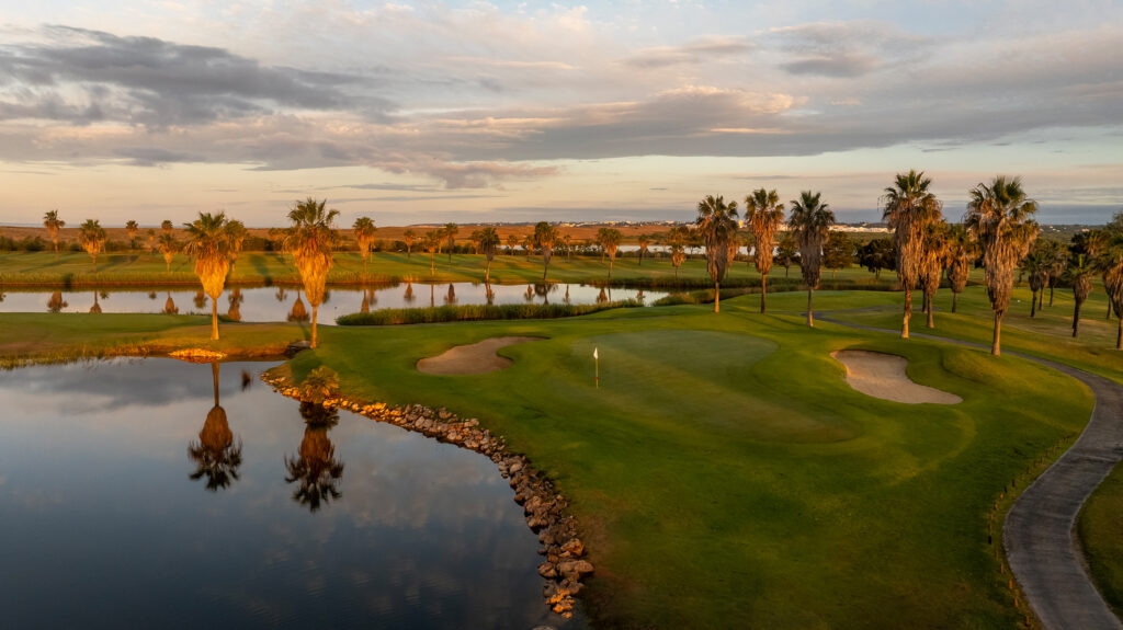 A green with bunkers and water hazards surrounded by palm trees at Salgados Golf Course