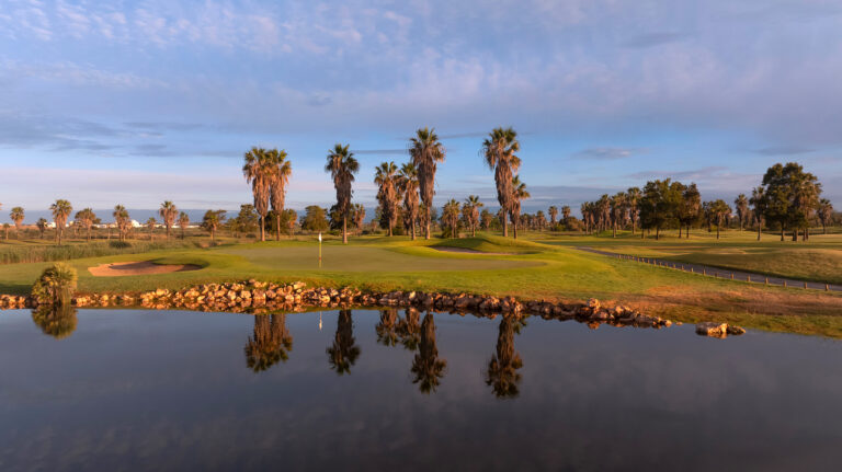 Lake with hole in background with a bunker and palm trees at Salgados Golf Course