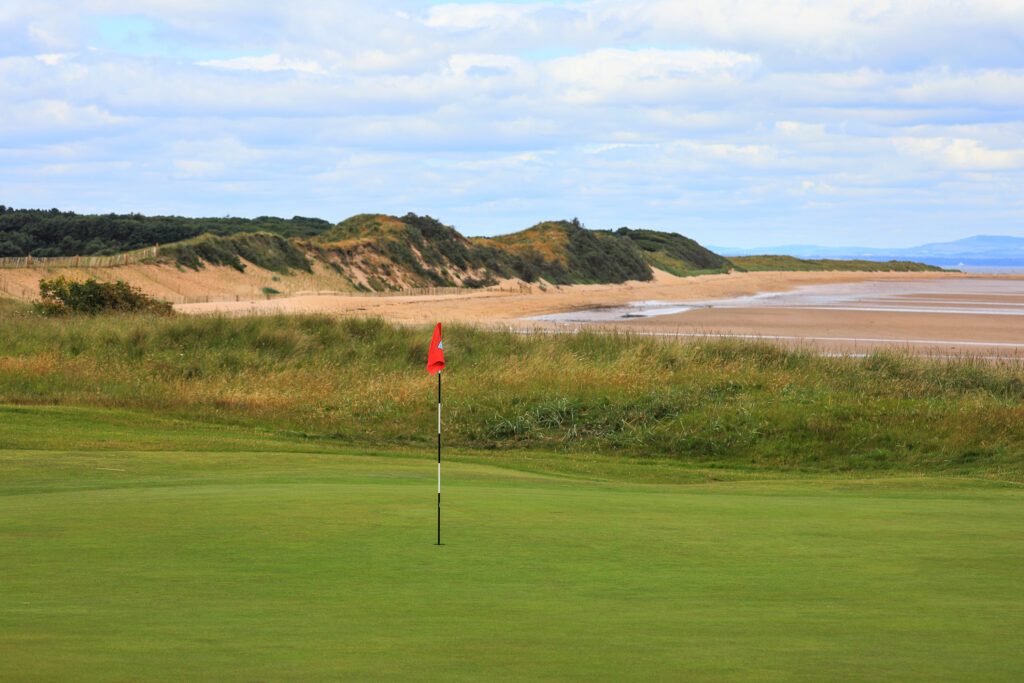 Hole with red flag at North Berwick Golf Club with beach in background