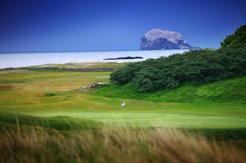 Hole with white flag at North Berwick Golf Club with ocean in background