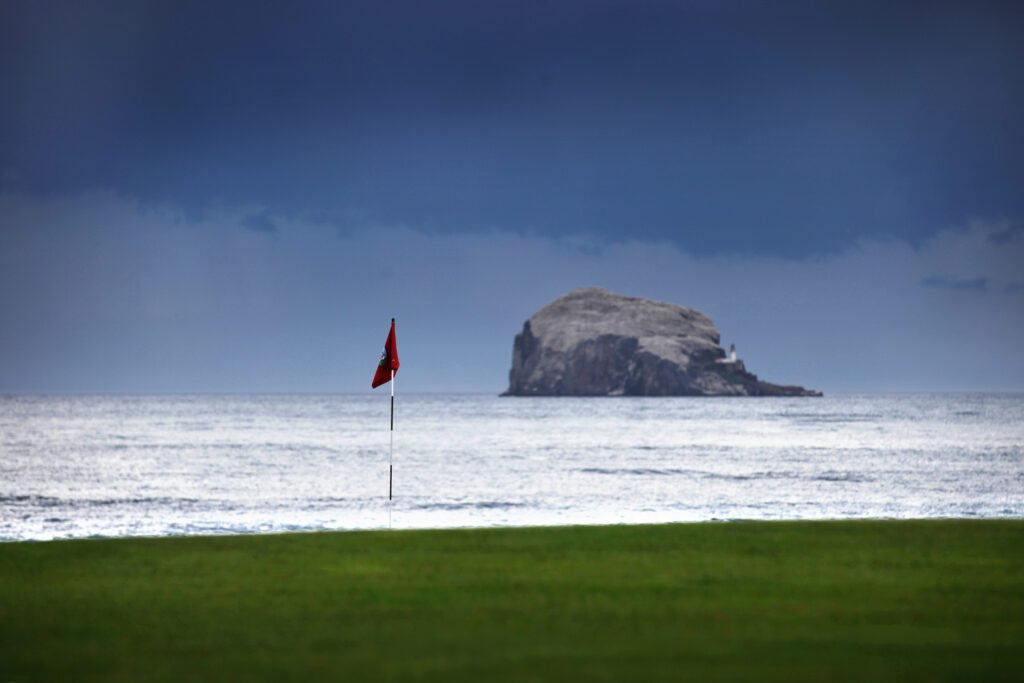 Hole with red flag at North Berwick Golf Club with ocean in background