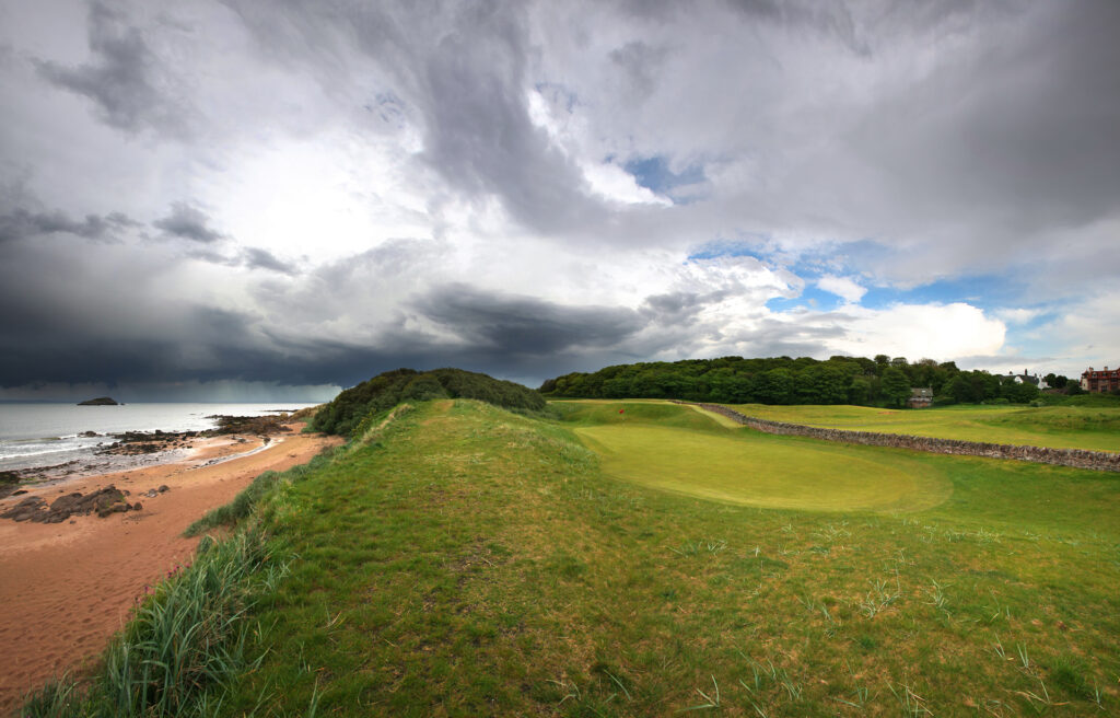 Hole with red flag at North Berwick Golf Club with beach view