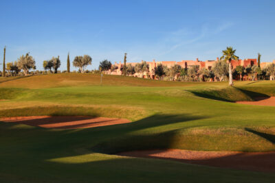 Hole with bunkers at Palm Golf Ourika with buildings in background