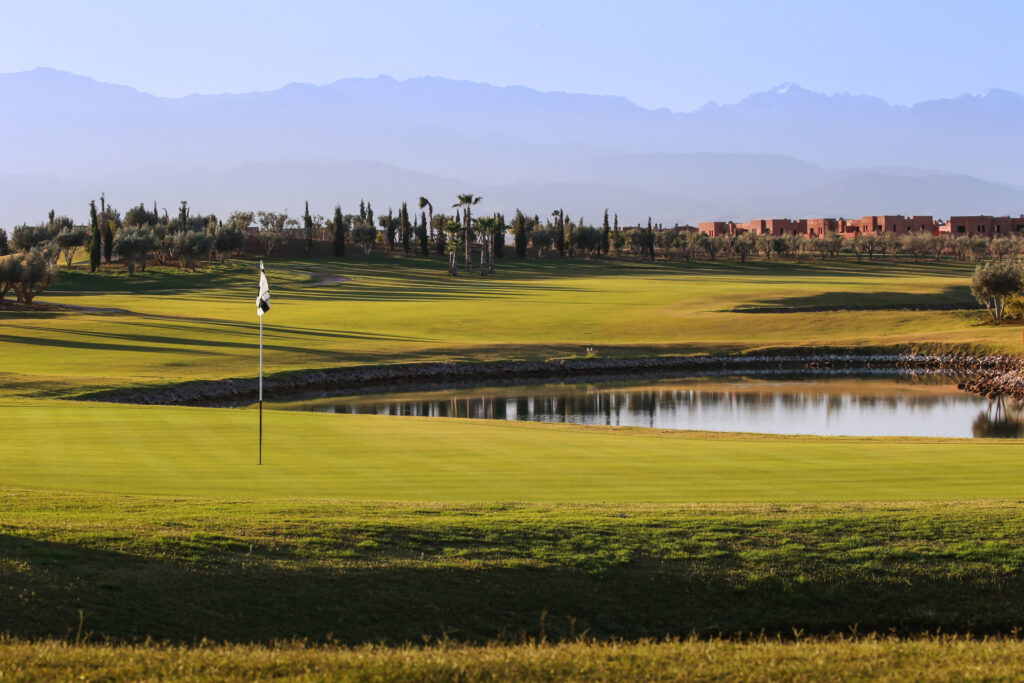 Hole with water hazard at Palm Golf Ourika with trees and buildings in background