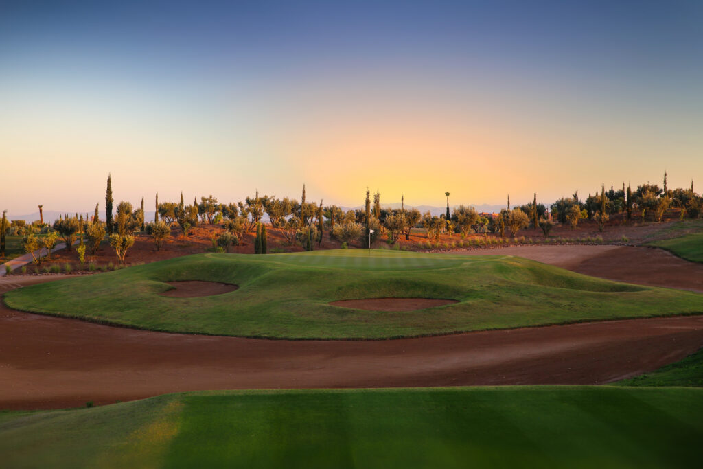 Hole with bunkers around at Palm Golf Ourika with trees in background at sunset