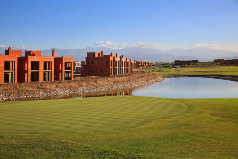 Hole with lake at Palm Golf Ourika with buildings around