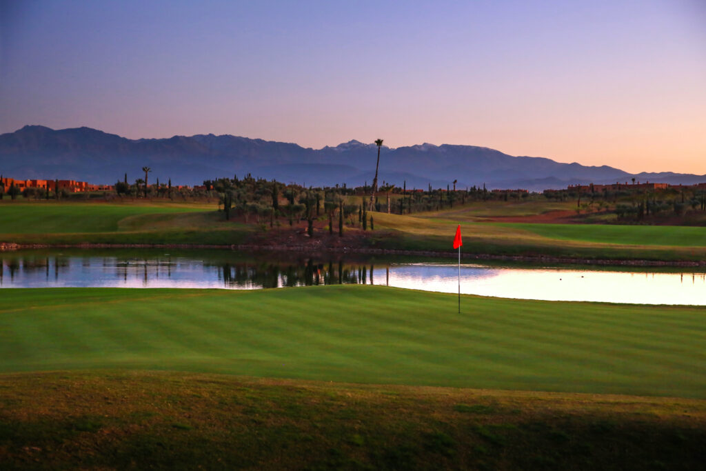 Hole with lake in background at Palm Golf Ourika with trees and mountains in background