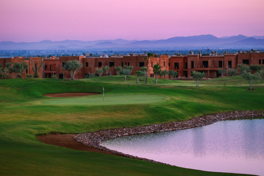 Hole with bunker and lake at Palm Golf Ourika with buildings in background