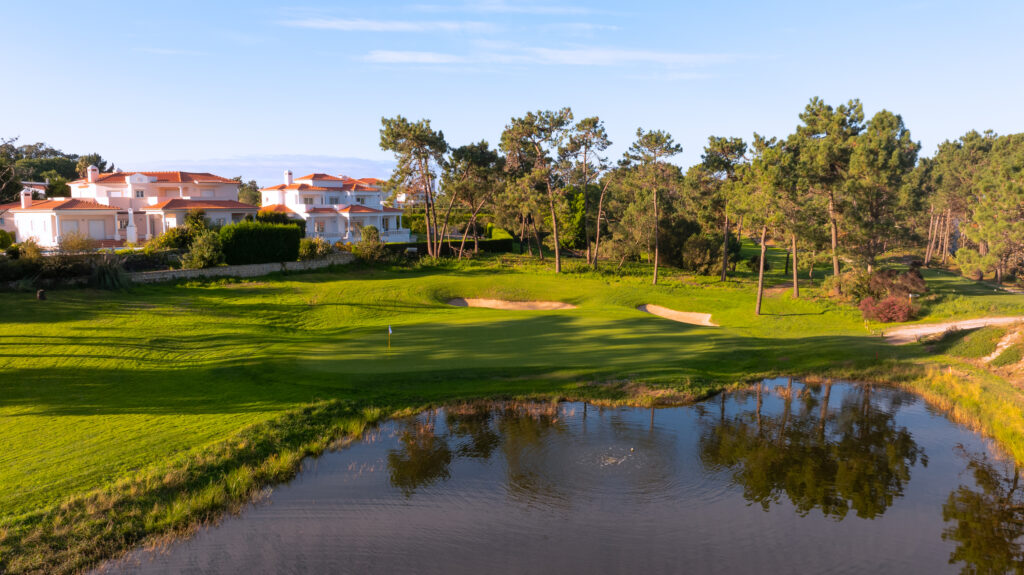 A hole with bunkers and a water hazard with buildings in the background at Praia d'el Rey Golf Course