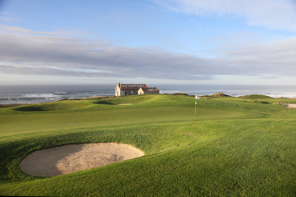 A green with a white flag and a bunker at Praia d'el Rey Golf Course