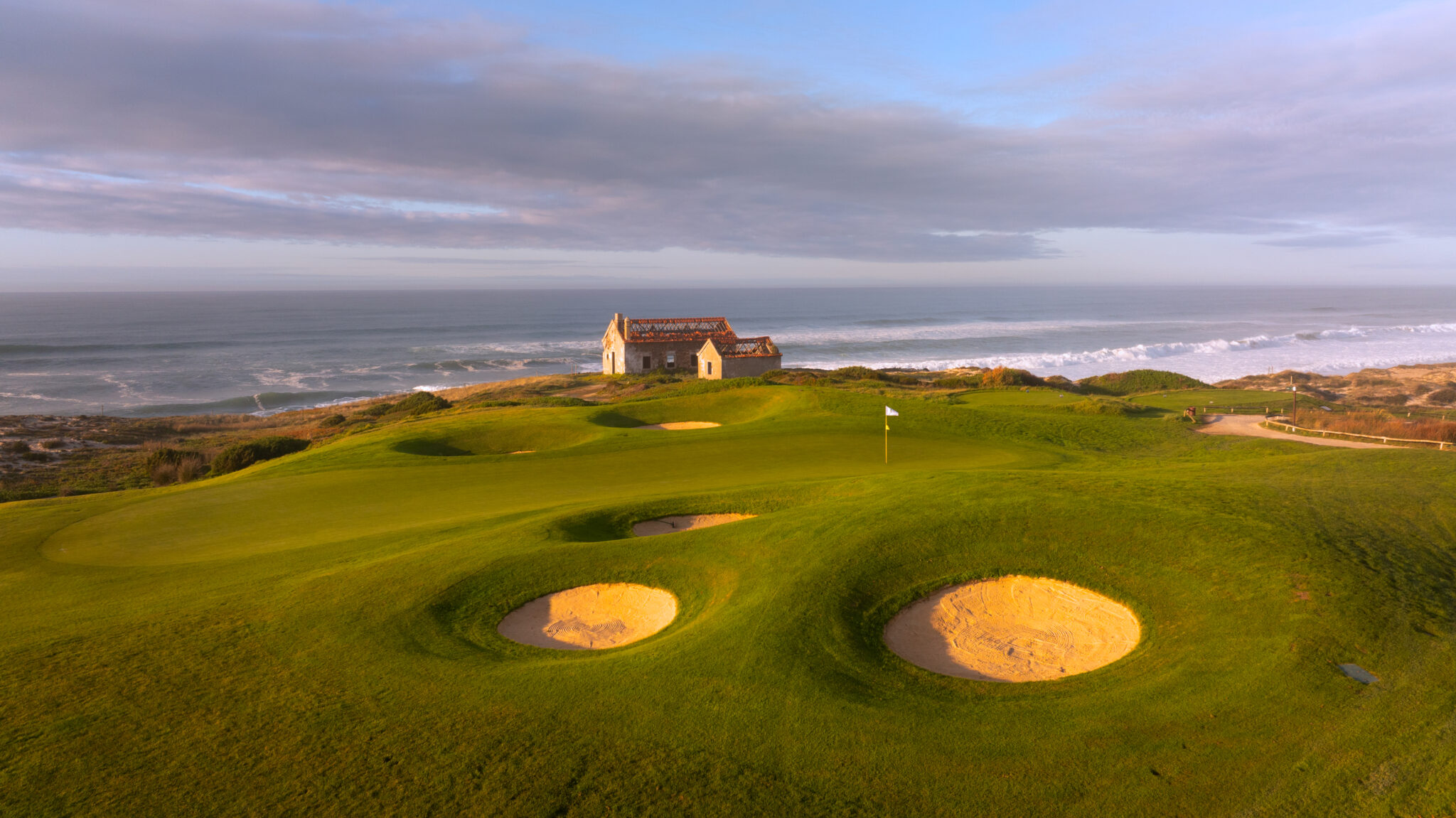 A hole with white flag and bunkers with beach view in background at Praia d'el Rey Golf Course