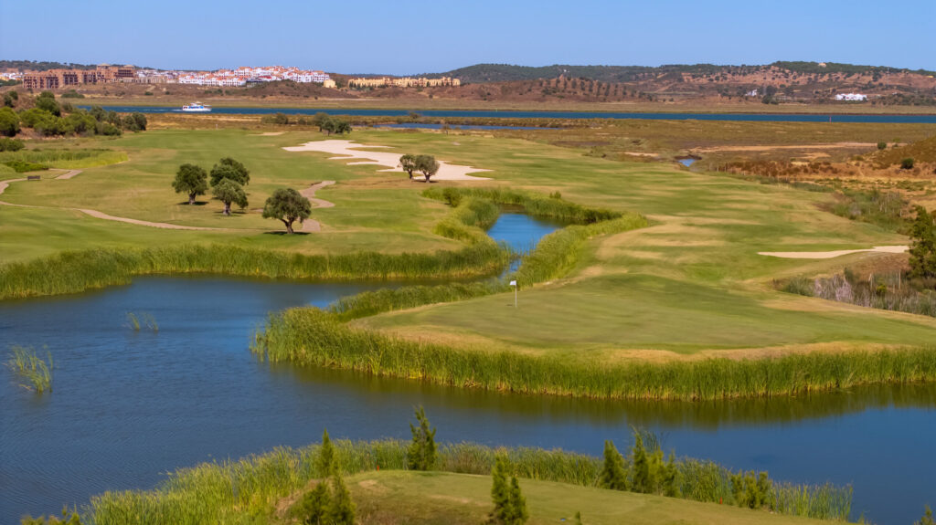 A green at Quinta do Vale Golf Course by a lake with hills and buildings in distance