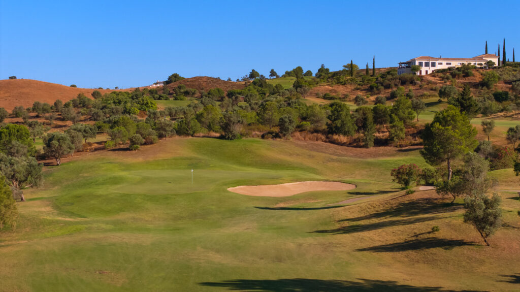 A green at Quinta do Vale Golf Course with a bunker and hillsides around