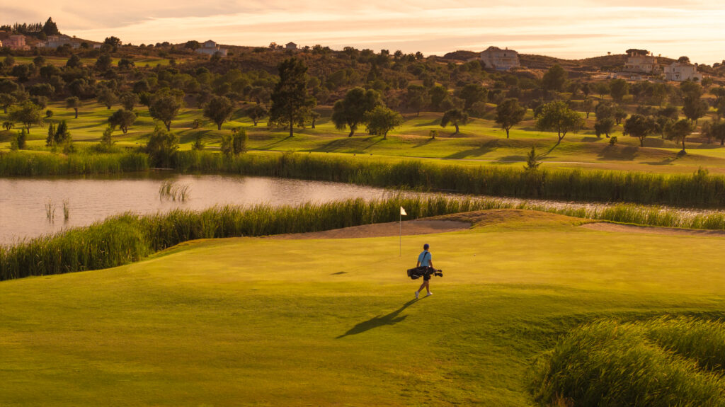 Person playing golf at Quinta do Vale Golf Course with lake in background at sunset