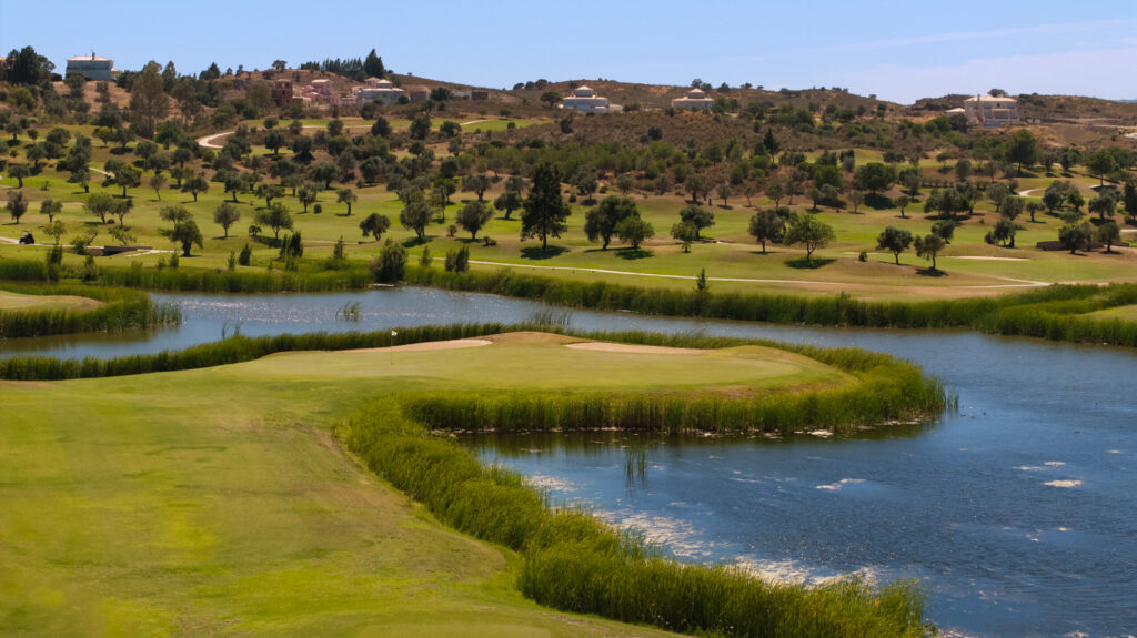 A green at Quinta do Vale Golf Course by a lake with trees in background