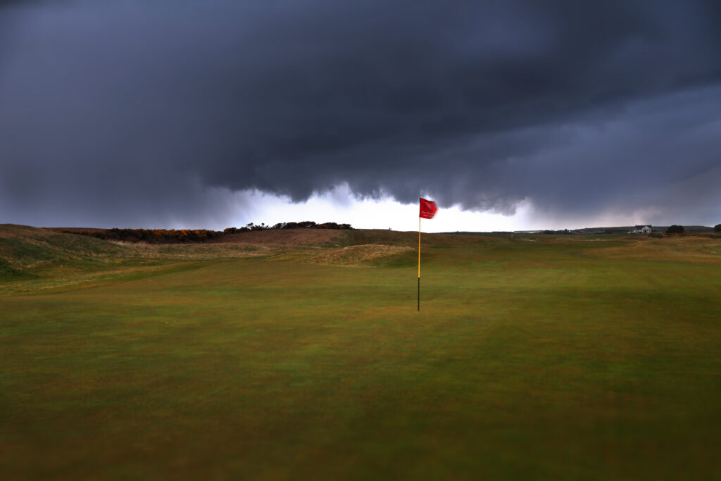 Hole with red flag at Balgownie Links at Royal Aberdeen Golf Club with stormy sky