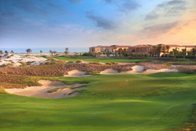 Hole with bunkers around at Saadiyat Beach Golf Club with buildings in background