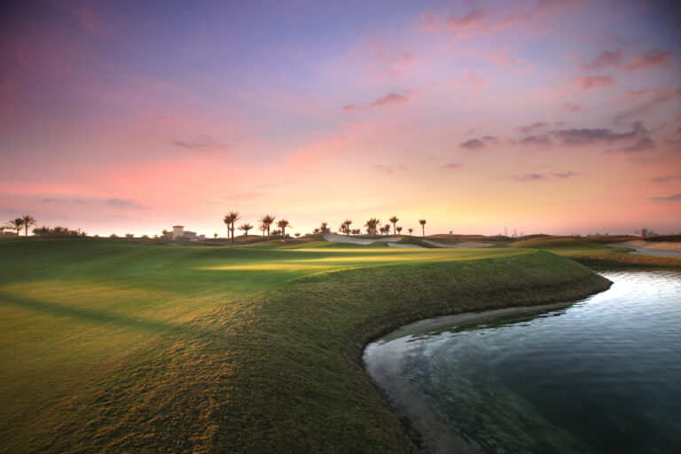 Fairway with lake next to it and palm trees in distance at Saadiyat Beach Golf Club