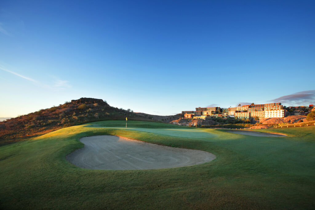 Hole with bunkers with hillsides around at Salobre Golf - Old Course with buildings in background