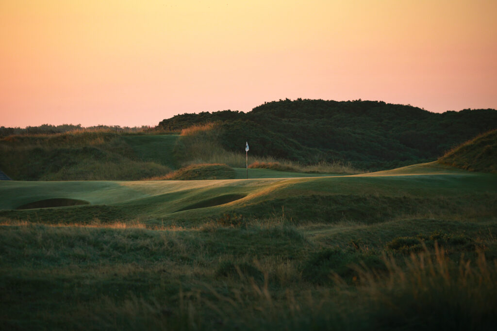 Hole with white flag and bunkers at The Castle Course at St Andrews with hills in background