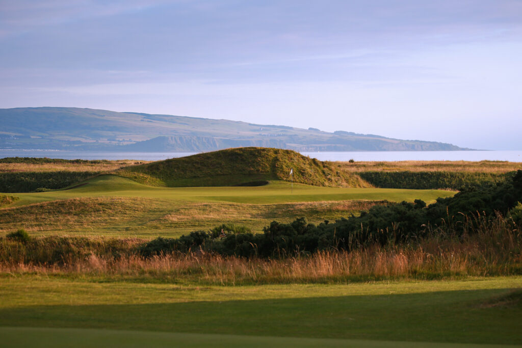 Hole with whtie flag at The Castle Course at St Andrews with ocean and hills in background