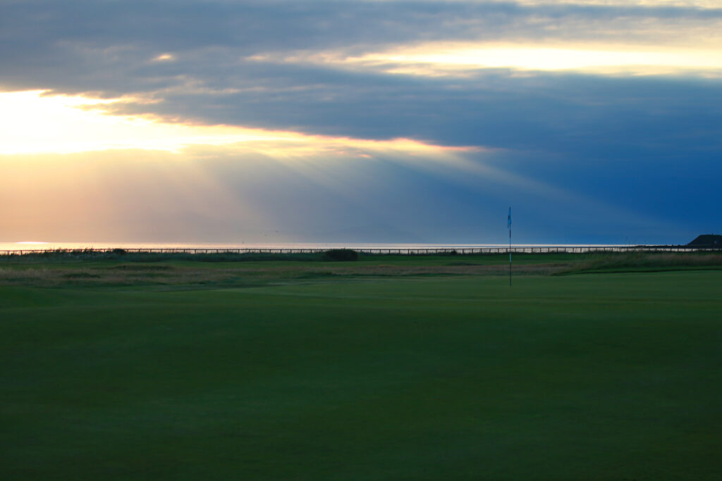 Hole with white flag at The Castle Course at St Andrews with sun shining through clouds