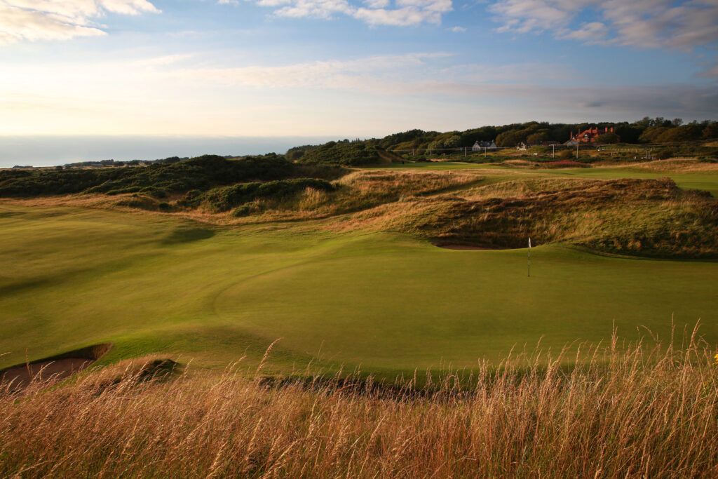 Hole with white flag at The Castle Course at St Andrews with buildings in distance