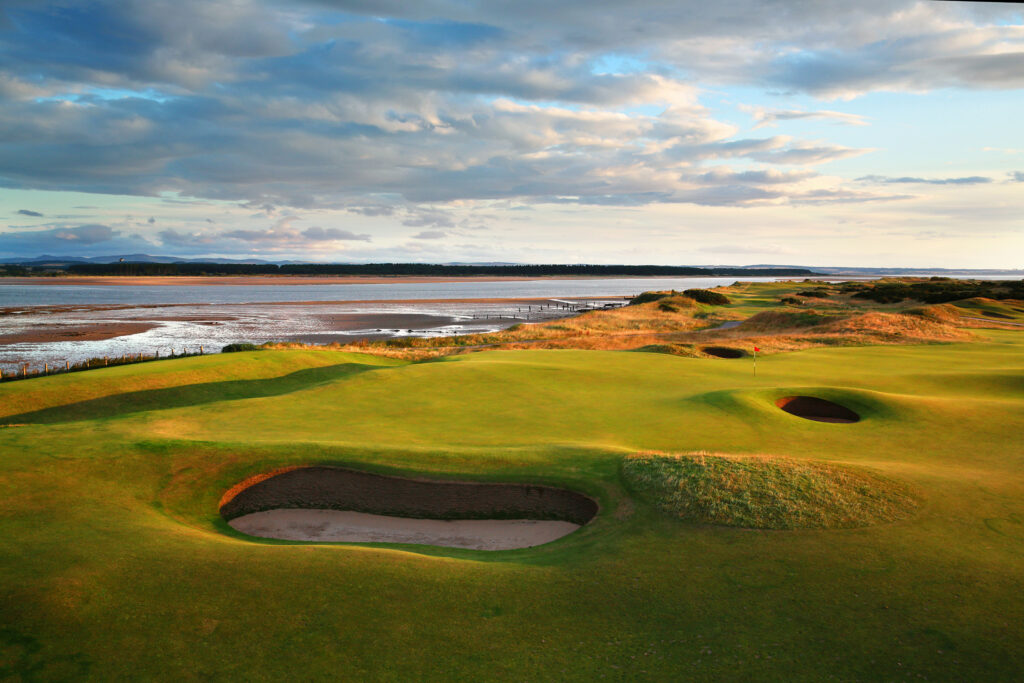 Hole with red flag and bunkers at The Old Course at St Andrews with ocean in background