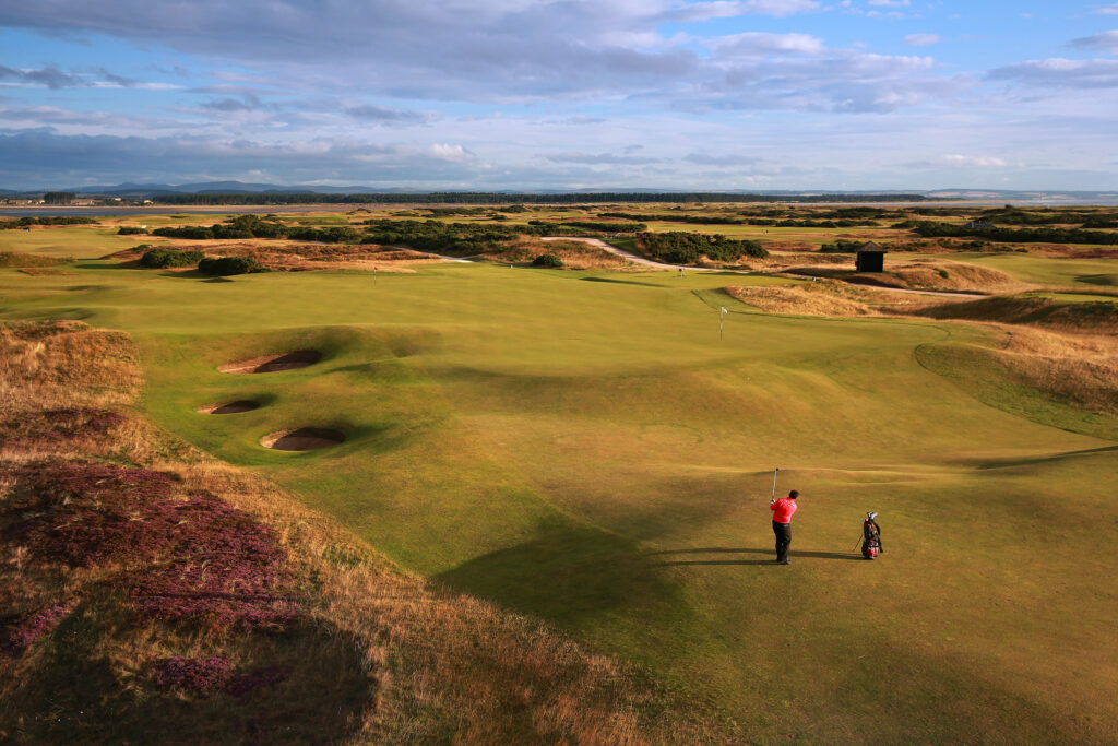 People playing golf at The Old Course at St Andrews on a fairway leading to a hole with bunkers