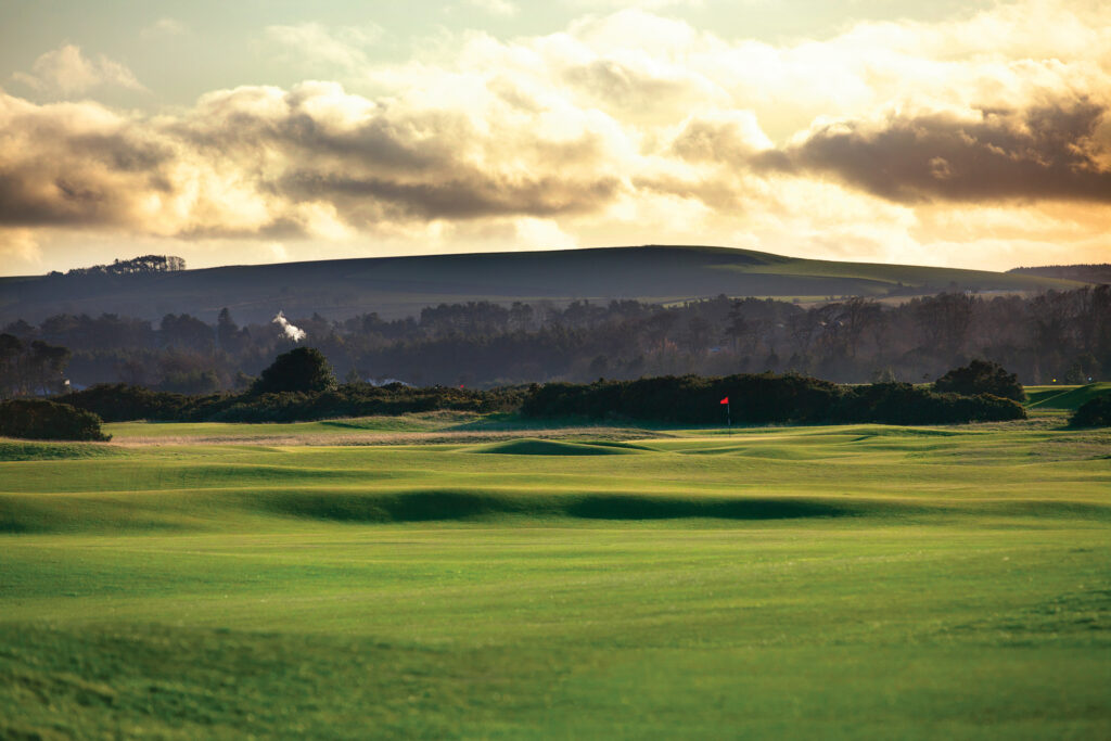 Fairway leading to hole with red flag at The Old Course at St Andrews with hills and trees in background