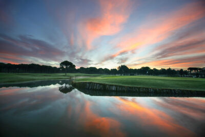 Fairway with lake and trees in background at Sueno Golf Club - Dunes Course at sunset