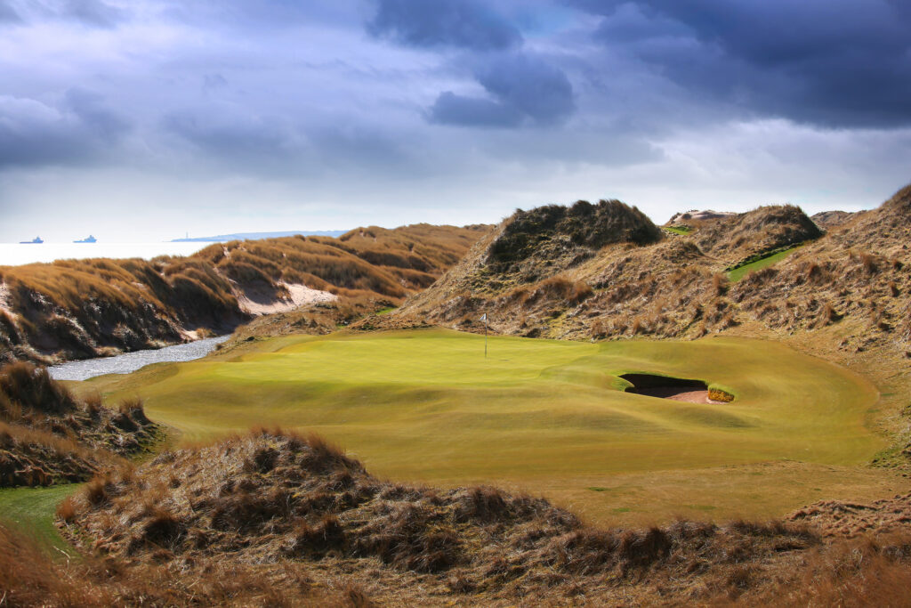 Hole with bunker and mounds around at Trump International Golf Links with river running next to it