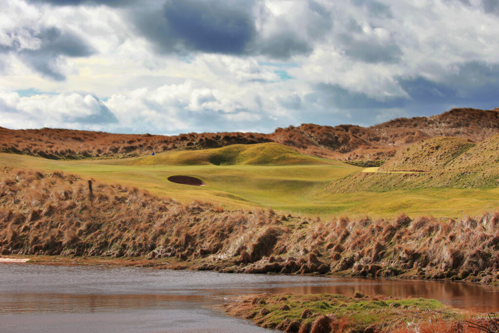 Hole with bunker at Trump International Golf Links with mounds in background and lake in foreground