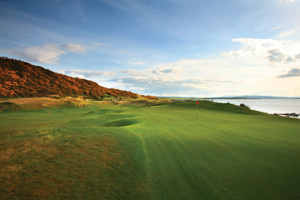 Hole with red flag at Castle Stuart Golf Links with ocean view