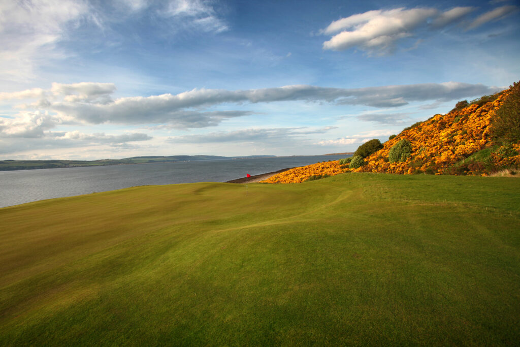 Hole with red flag at Castle Stuart Golf Links and ocean view