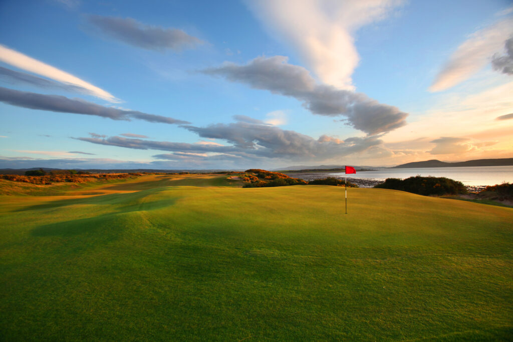 Hole with red flag at Castle Stuart Golf Links with ocean view