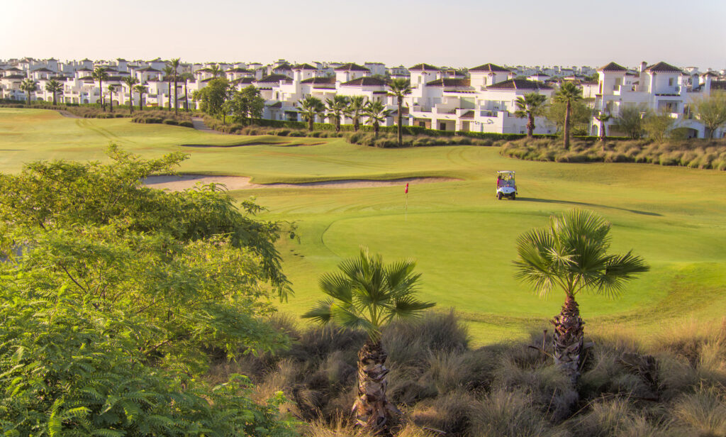 A hole with buildings in background with buggy at La Torre Golf Course