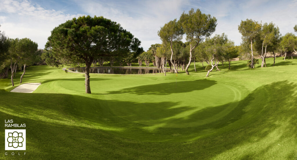 A hole with a yellow flag at Las Ramblas Golf Course with a lake in the background