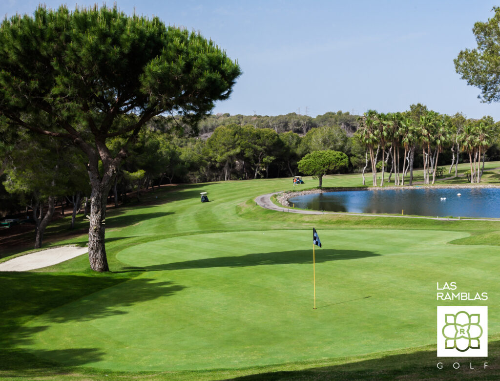 A hole with a black and white flag with a lake in the background at Las Ramblas Golf Course