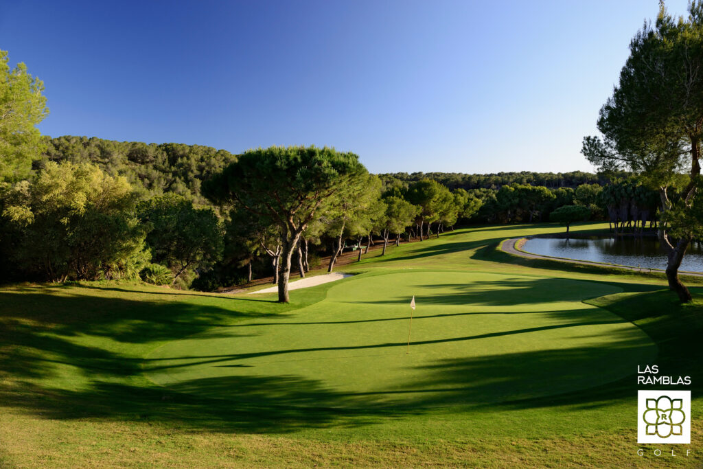 A hole with a white flag and a lake in the background at Las Ramblas Golf Course