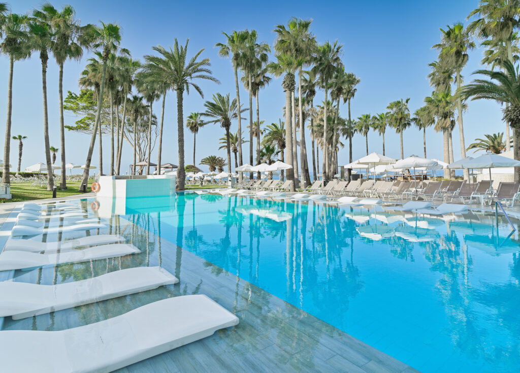 Outdoor pool at Leonardo Plaza Cypria Maris with loungers and palm trees around