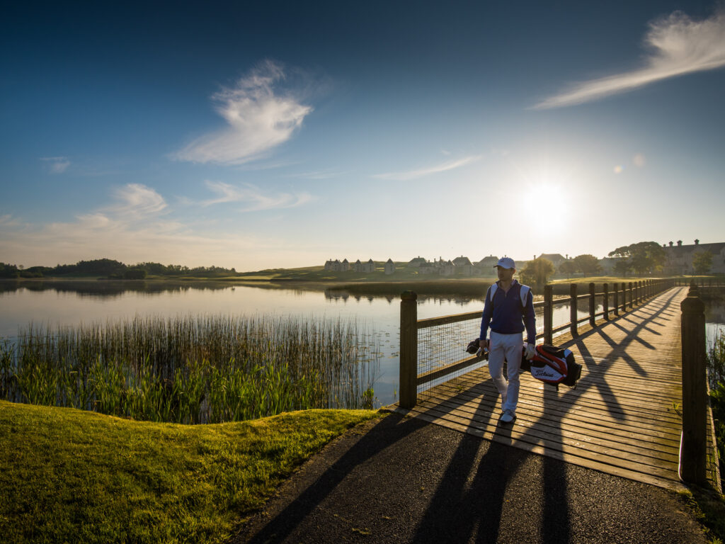 Person walking over a lake at Lough Erne Resort with their golf bag