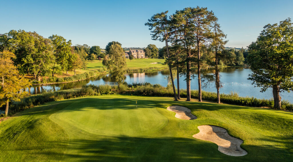 Hole with bunkers and trees around at Malone Golf Club with lake in background