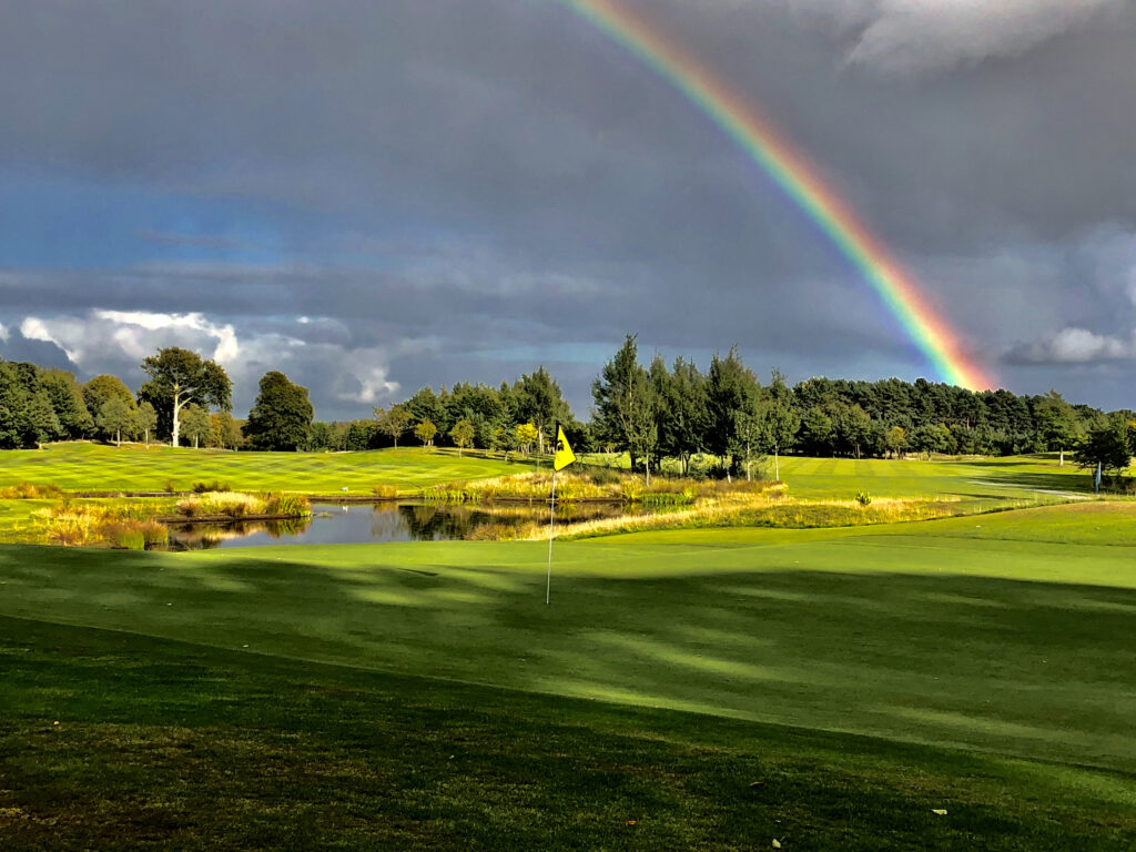 Hole with yellow flag at Meldrum House Golf Club with a rainbow