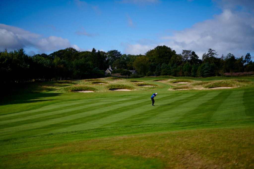 Person playing golf at Meldrum House Golf Club with bunkers and trees in background